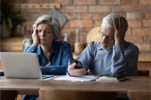 Unhappy mature couple checking financial documents, calculating domestic bills, having problem with money, upset senior man wearing glasses and woman feeling depressed about bankruptcy or debt