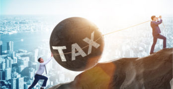 Two men in business suits struggling to roll a giant stone ball labeled "tax" up a steep hill.
